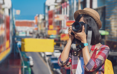 Woman photographer is taking images with dslr camera. Photographer covering her face with the camera. Happy woman on vacation photographing with a dslr camera in the city. Vacation photography travel