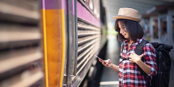 Young trendy woman using smartphone at the train station. Young woman waiting on station platform on background moving train using smart phone. Tourist text message and plan route of stop railway