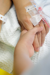 Close-up of kid holding the hand of a woman with IV drip at the hospital