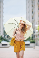 Young woman suffering from heat in the city, she is walking with parasol and wiping sweat from her forehead