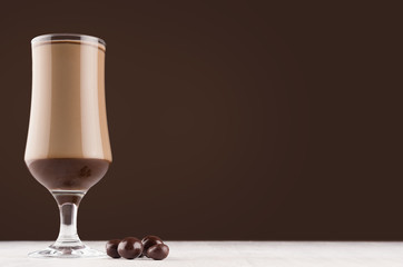 Cappuccino coffee cocktail with chocolate candies on dark brown wall and white wood board.