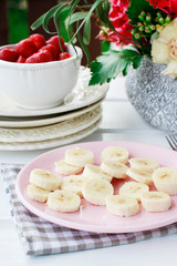 Sliced bananas and ripe strawberries on the table. Bouquet of flowers