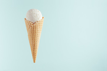 White creamy ice cream in crisp waffle cone on soft light pastel green background, mock up, copy space.