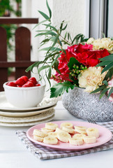 Sliced bananas and ripe strawberries on the table. Bouquet of flowers