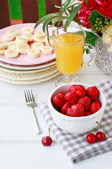 Bowl of strawberries, sliced bananas on pink plate and glass of orange juice on the table