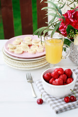 Bowl of strawberries, sliced bananas on pink plate and glass of orange juice on the table