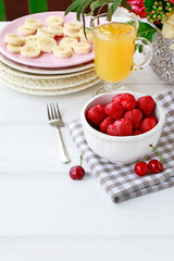Bowl of strawberries, sliced bananas on pink plate and glass of orange juice on the table