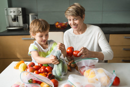 smiling senior woman and child grandson with vegetables in eco cotton bags at home. zero waste shopping concept. - Powered by Adobe