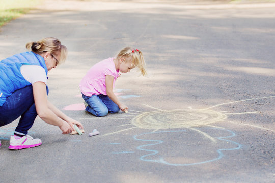 mother and  girl draws with chalk on  pavement
