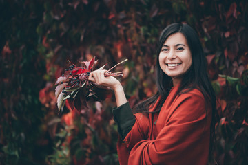 Joyful beautiful girl with long natural black hair on autumn background of green red grape hedge....