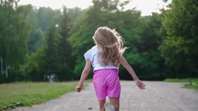 Back view of a girl running in the park. Happy little girl with long hair having fun alone on the natural green background in summer.