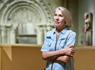 Mature woman visitor in historical museum looking at art object.