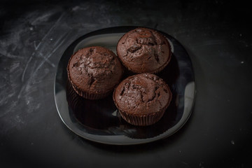 Three chocolate muffins on a black plate on a dark background close up