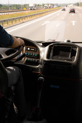 A Caucasian male driving an old bus along highway, asphalt road surface illuminated by bright daylight, cars seen in the horizon.