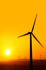 Obraz premium silhouetted windmills on hill over orange colored sunrise sky
