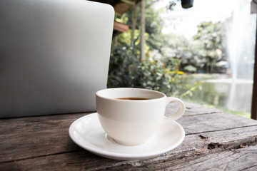 A cup of coffee on the wooden table behide laptop