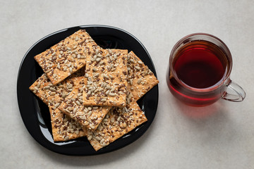 Cup of tea and cereal cookies on table. Homemade pastry on black plate. Healthy food, top view. Breakfast concept. Cookies with seeds. Laconic design.