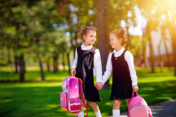 Portrait of happy Caucasian young smiling girls wearing school backpack outside the primary school. schoolgirl, elementary school student going from school, graduation, summer holidays.