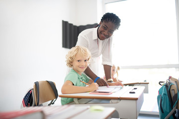 Obraz premium Pleasant dark-skinned teacher standing near pupil