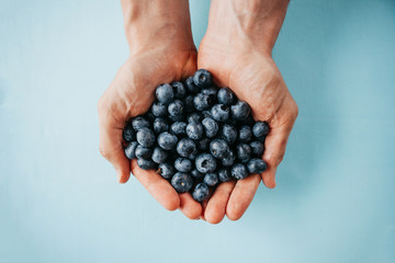 Closeup man holds blueberries in hands on a blue background. Source of vitamins and diet food or berries.