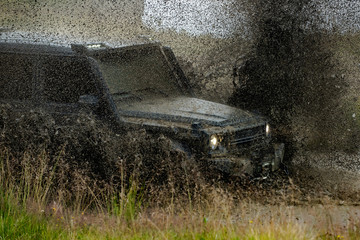 Low angle view of front of SUV on mountain road. Water splash in off road racing. Off-road 4x4 concept. Wheel close up in a countryside landscape with a muddy road. © Volodymyr