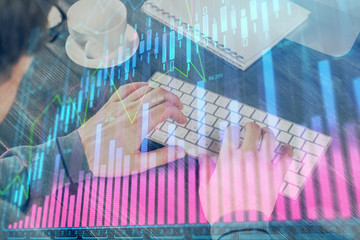 Double exposure of graph with man typing on computer in office on background. Concept of hard work.
