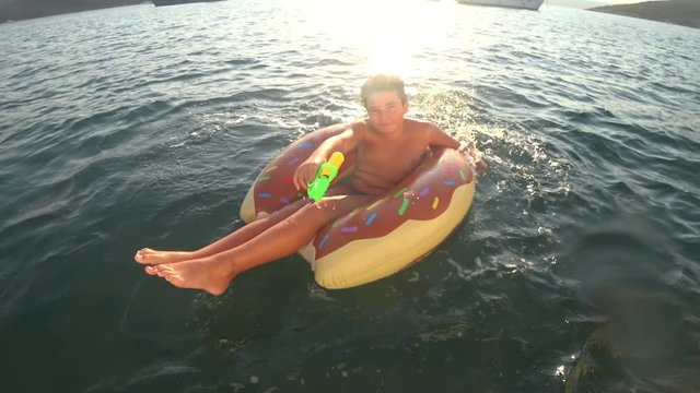 Summer on the Mediterranean deep blue sea young boy floating on an air mattress at summer vacation. Teenager playing with squirt gun in a sea   Holiday, travel, people, adventure, tourism concept