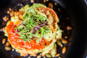 A dish of vegetable patties, Halloumi and Avocado, stacked up on a dark blue plate.