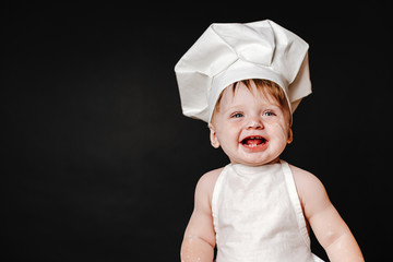 Charming toddler baby in hat of cook and apron laughing happily