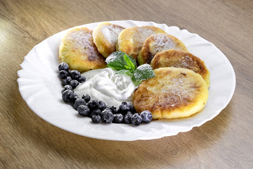 cheesecakes with sour cream and blueberries on a white plate with mint leaves on a wooden background