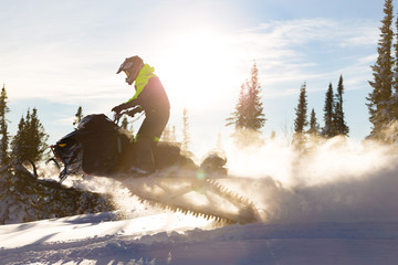 Snowmobile jump in backlight. Gold plumes and whirlwinds from a snowmobile in a jump among the...