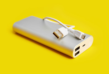 Power bank for charging mobile devices. White smart phone charger with power bank. Battery bank on a yellow background . External battery for mobile devices.