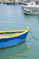 Fototapeta na wymiar Small blue fishing boat in the clean water, water bay in Marsaxlokk, Malta's largest fishing village 