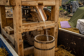 Fototapeta na wymiar old wooden mill medieval technology with falling chopped flour into barrel, historical open air festival event 
