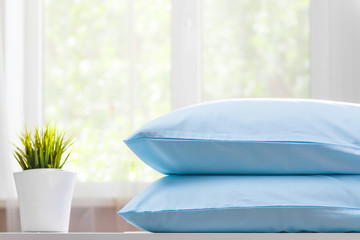 Closeup of two blue pillows lie on a dresser against the background of a blurred window