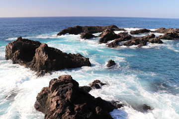 Fototapeta na wymiar Blue ocean water crashing over rocks at a beach in Los Gigantes, Spain