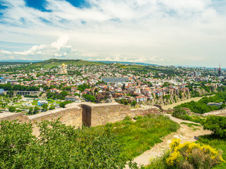 Great view from Narikala fortress in Tbilisi in the middle of the day. Kura river, Metekhi bridge, churches and old houses of the city seen among green trees.