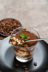 Portion of Classic tiramisu dessert in a glass cup on concrete background