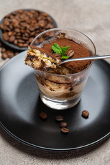 Portion of Classic tiramisu dessert in a glass cup on concrete background