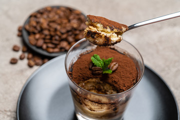 Portion of Classic tiramisu dessert in a glass cup on concrete background