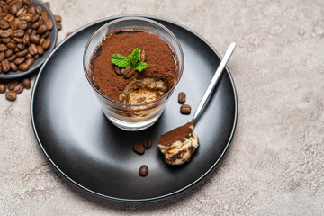 Portion of Classic tiramisu dessert in a glass cup on concrete background