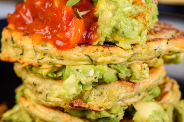 A dish of vegetable patties, Halloumi and Avocado, stacked up on a dark blue plate.