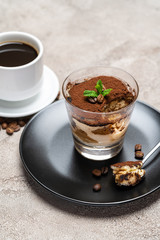 Portion of Classic tiramisu dessert in a glass cup and espresso coffee on concrete background