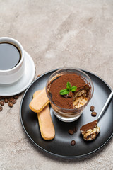 Portion of Classic tiramisu dessert in a glass cup and espresso coffee on concrete background