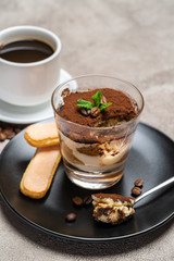 Portion of Classic tiramisu dessert in a glass cup and espresso coffee on concrete background