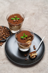 Portion of Classic tiramisu dessert in a glass cup on concrete background