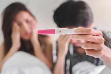 Unhappy couple young asian woman and man holding pregnancy test showing a positive result, Wellness...