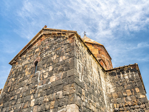 Ancient stone walls of Surp Arakelots (Holy Apostles) church, part of Sevanavank monastic complex in Armenia, shot against blue sky with clouds in summer.