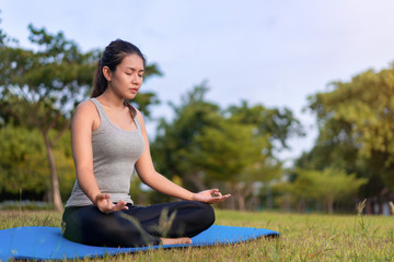 Fototapeta na wymiar Asian woman meditating and sit in the lotus pose at park, Healthy and Yoga Concept,Mind-body improvements concept, Selective focus, Copy space.