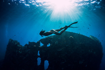 Freediver girl in pink swimwear with fins swimming underwater at wreck ship. Freediving in ocean